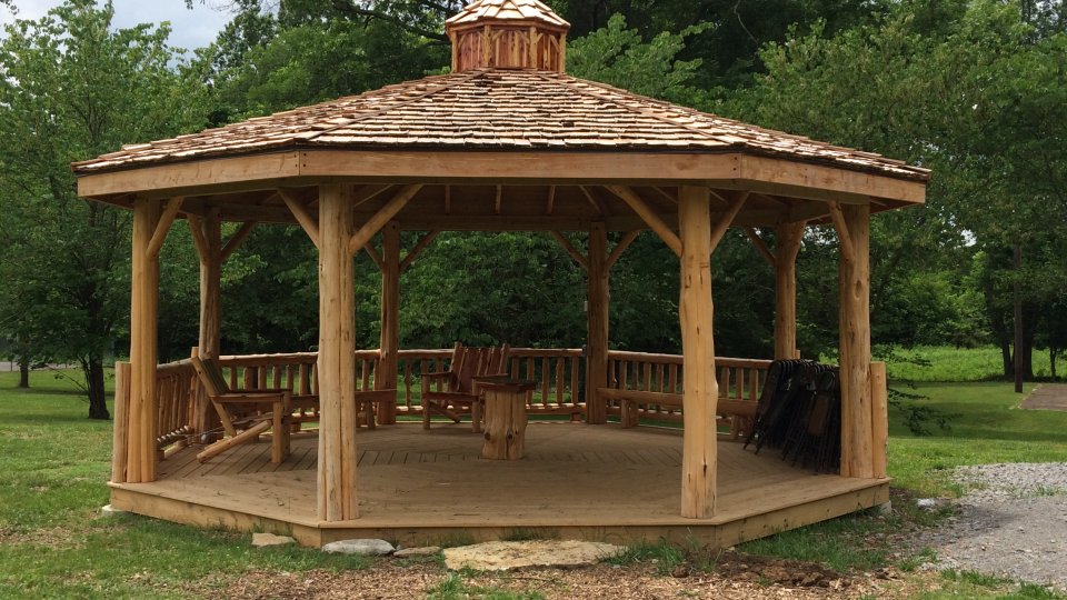 Wooden gazebo in a park with surrounding trees.