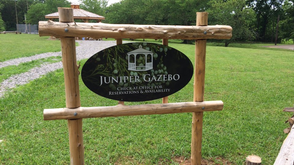 Juniper Gazebo sign with wooden frame on a grassy park background.