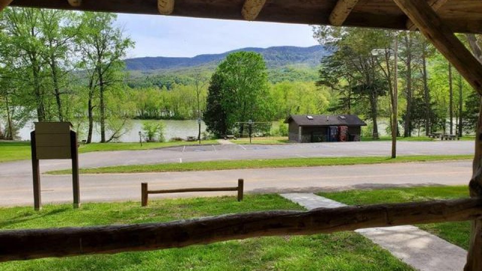 View from a shelter overlooking a serene lake with distant hills and lush greenery.