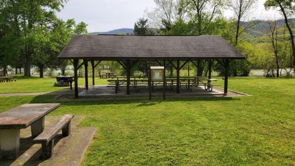 Outdoor park pavilion with picnic tables and green hills in the background.