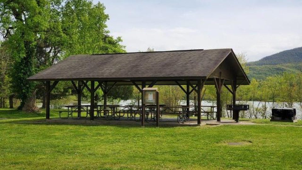 Open picnic shelter in a green park with mountains in the background.