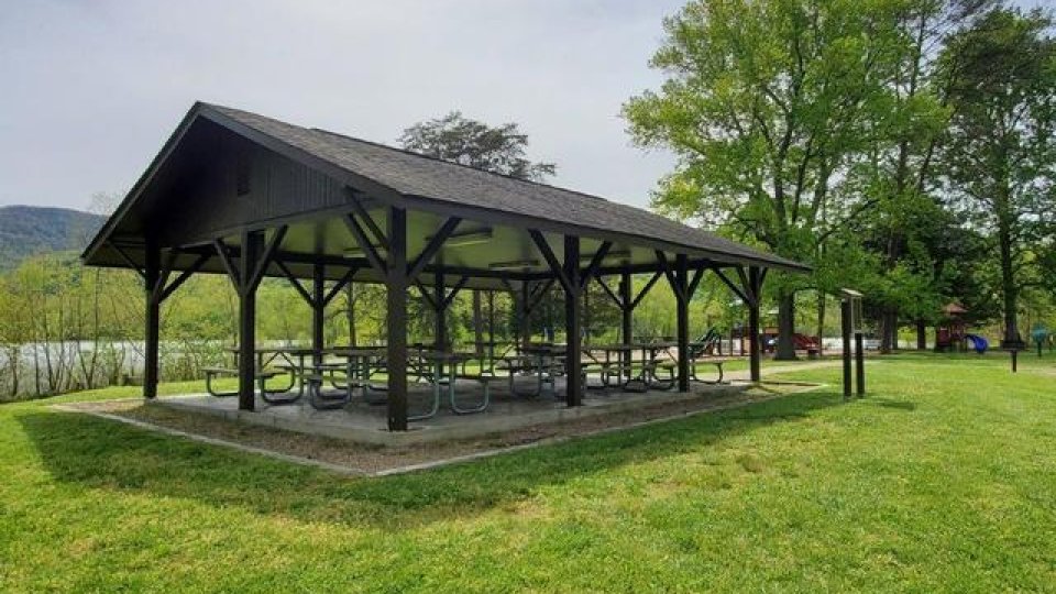 Open picnic shelter in a lush green park with mountains in the background.