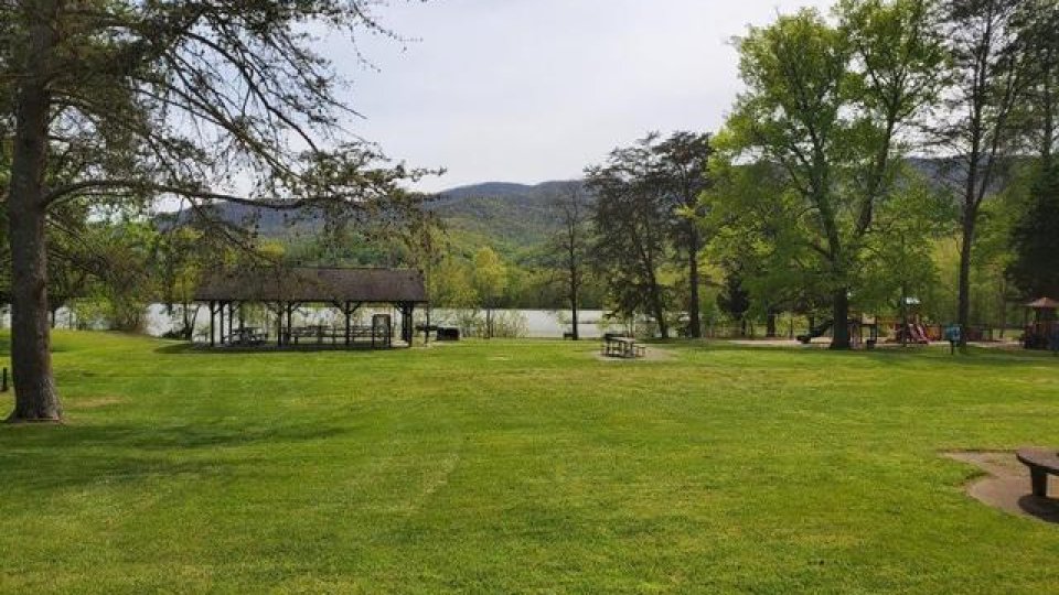 Scenic park with lush green grass, trees, and a gazebo by a lake.