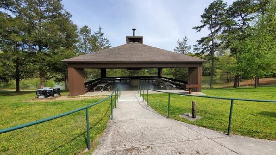 Pavilion in a park with a walking path leading to it, surrounded by trees and green grass.
