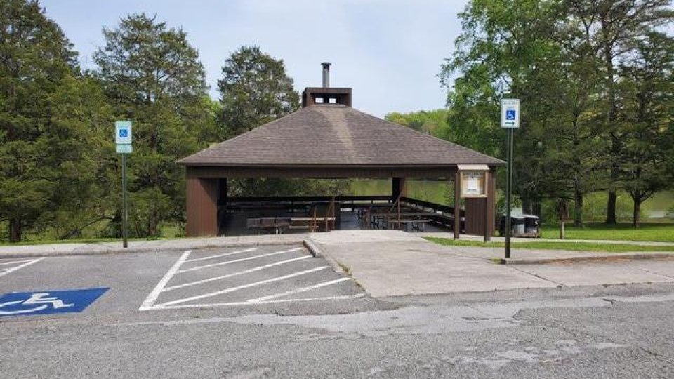 Parking lot with empty spaces in front of a small pavilion in a park.
