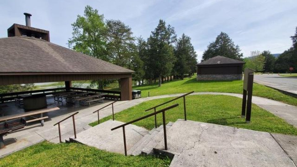 Outdoor park area with paved walkways, a pavilion, and green lawns under a blue sky.