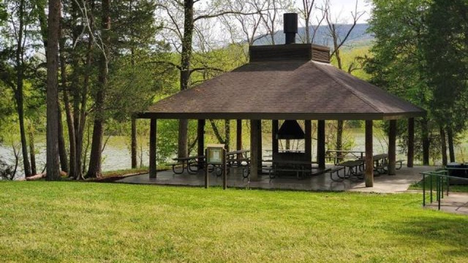 Wooden gazebo by a lake surrounded by trees and grass.
