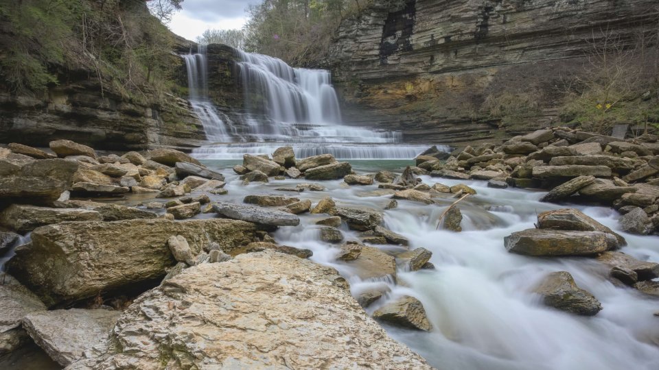 Cascading waterfall over rocky cliffs with fast flowing river.