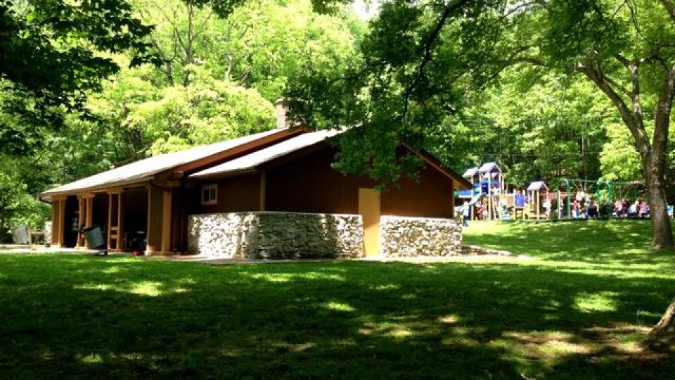 Stone cabin in a lush green park with children playing in the background.