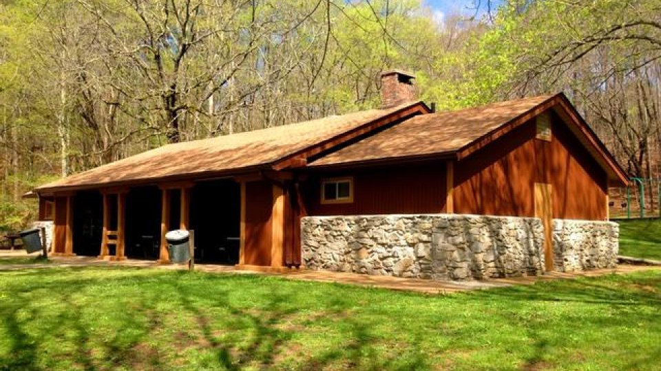 Rustic home with stone foundation surrounded by trees in daylight.