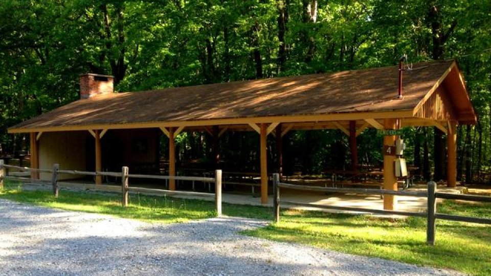 Wooden pavilion in a lush forest setting with a gravel path.