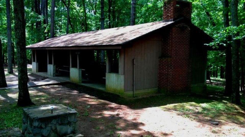 Small cabin in a forest with a large chimney and front porch.