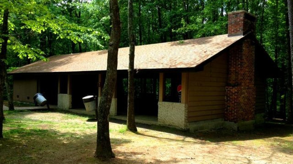Small cabin in the woods with a large chimney and covered porch.