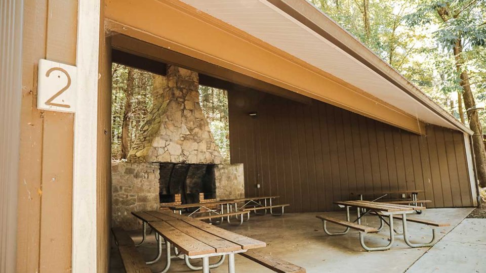 Covered picnic area with stone fireplace and wooden tables.