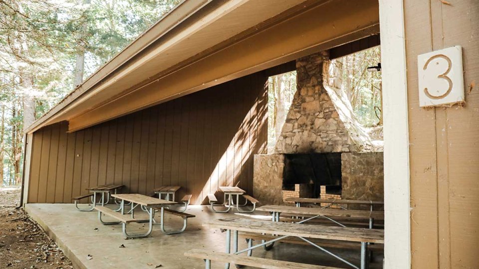 Outdoor pavilion with picnic tables and a large stone fireplace.