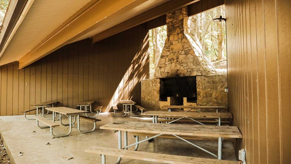 Covered picnic area with wooden tables and a stone fireplace.