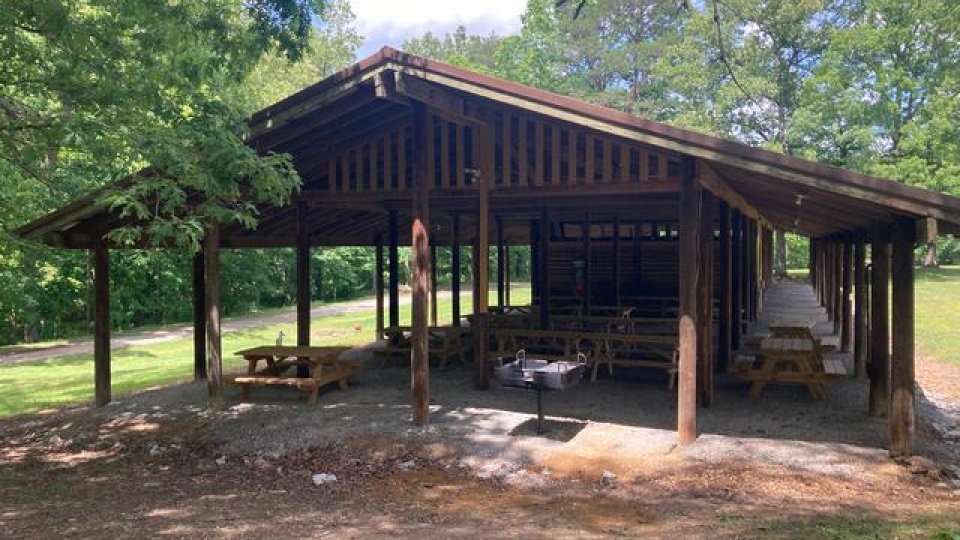 A wooden pavilion in a sunny park with picnic tables inside.