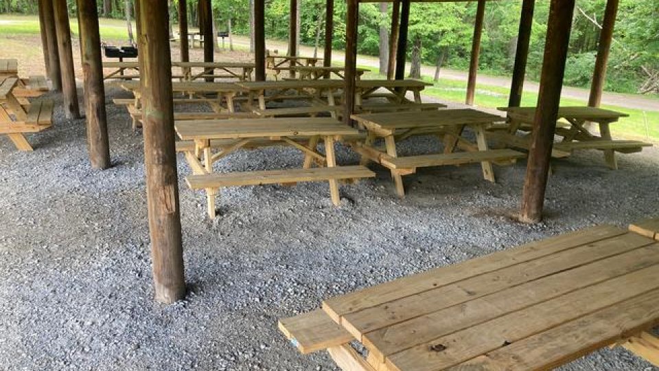 Sheltered picnic area with wooden tables on gravel.