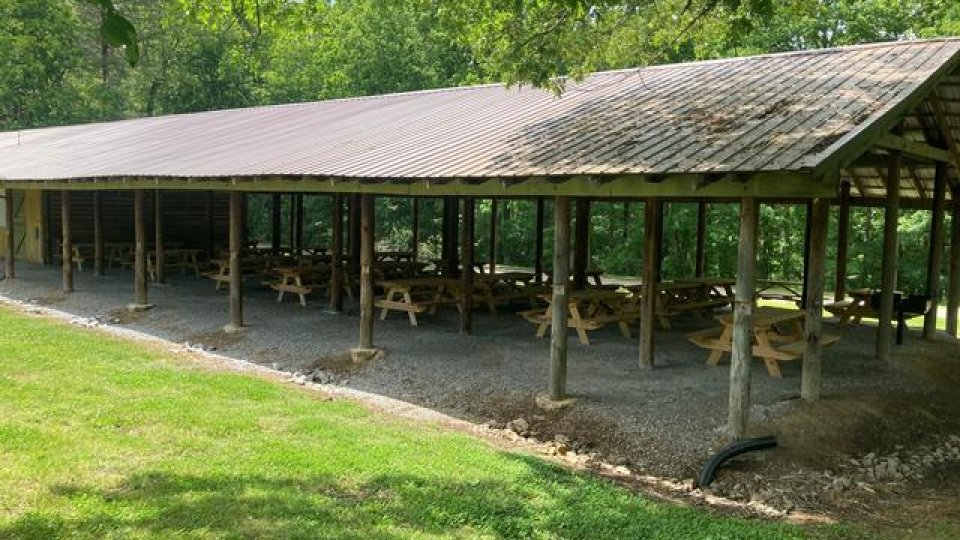 Open-sided picnic shelter with wooden benches in a park setting.