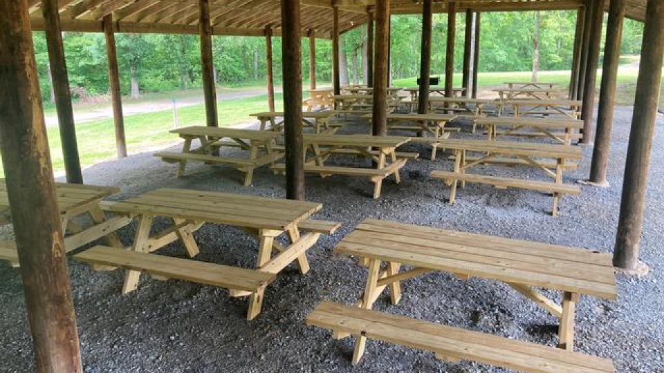 Covered picnic area with wooden tables and gravel floor in a park.