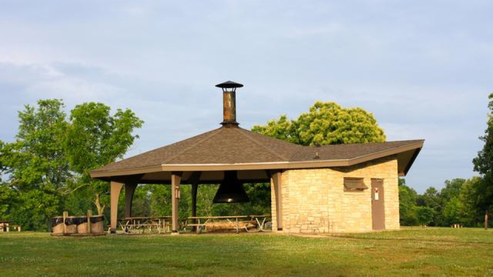 Park pavilion with chimney surrounded by lush green trees.
