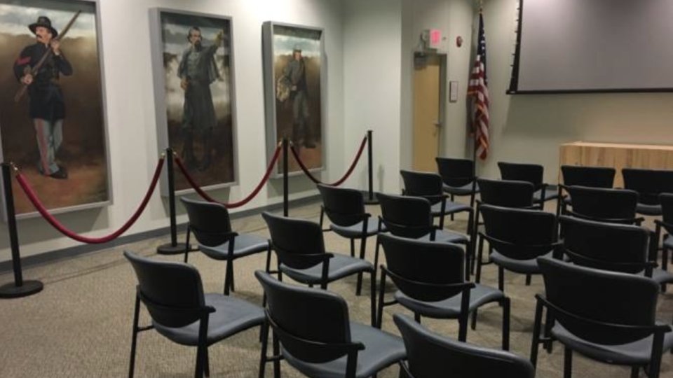 Conference room with empty chairs, paintings on walls, and a projector screen.