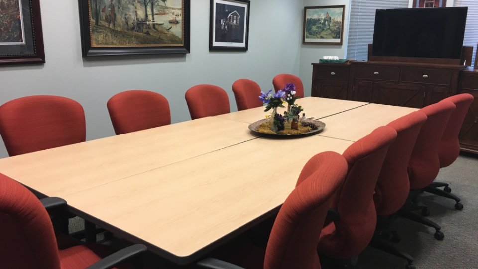 Meeting room with red chairs, a long table, and landscape paintings on the walls.