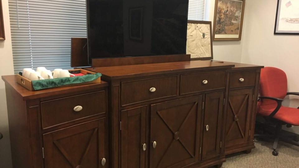 Dark wood cabinet with a large black TV on top, in an office setting.