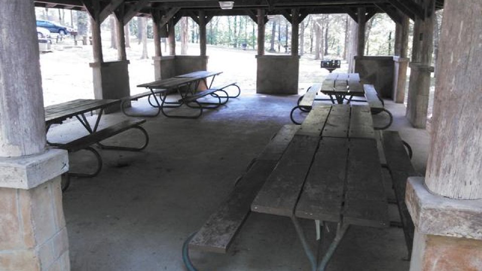 Shelter with several empty picnic tables and wooden beams.