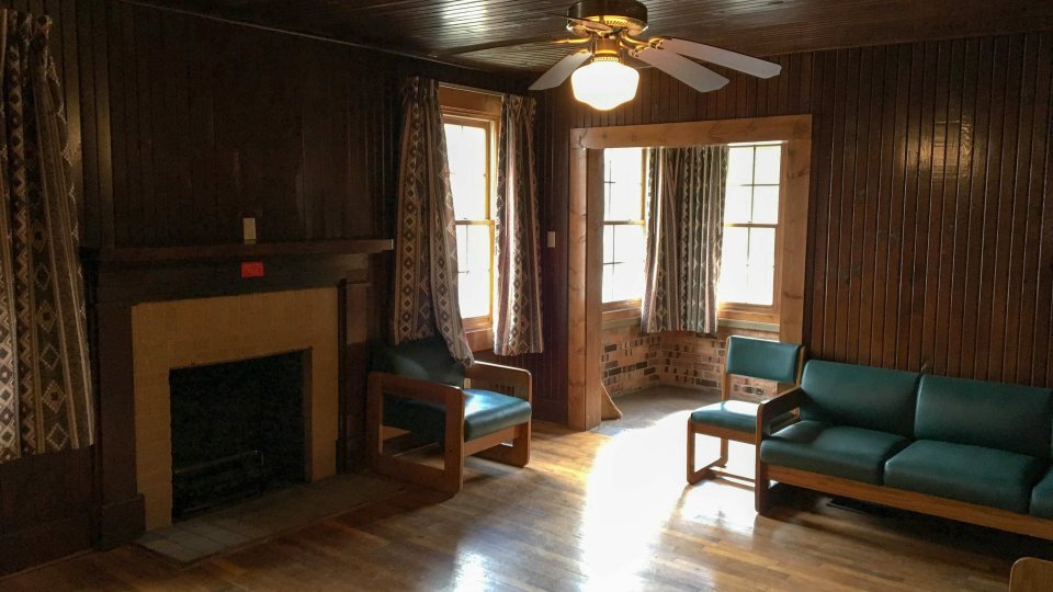 Cozy wooden living room with fireplace, chairs, and a ceiling fan.
