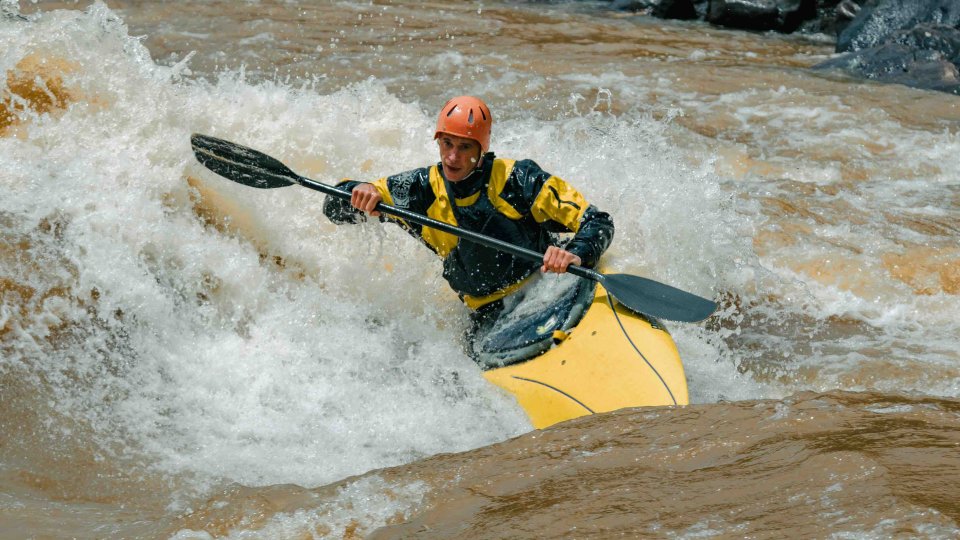Man kayaking through rough river rapids.