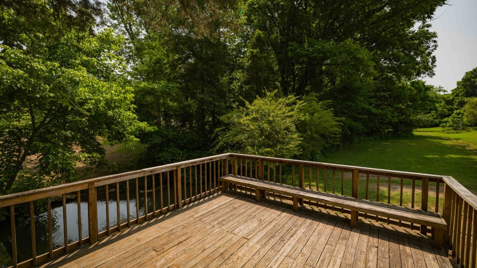 Wooden deck overlooking a verdant park with trees and a small creek.