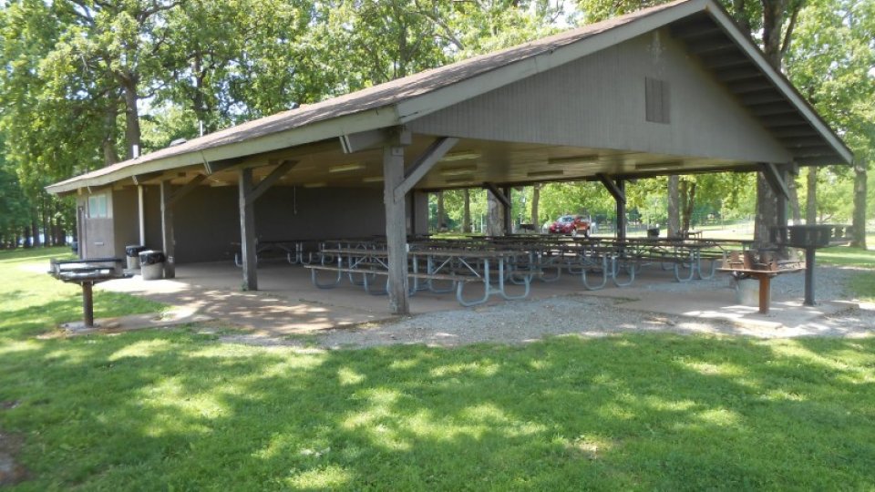 Pavilion with picnic tables in a sunny park setting.