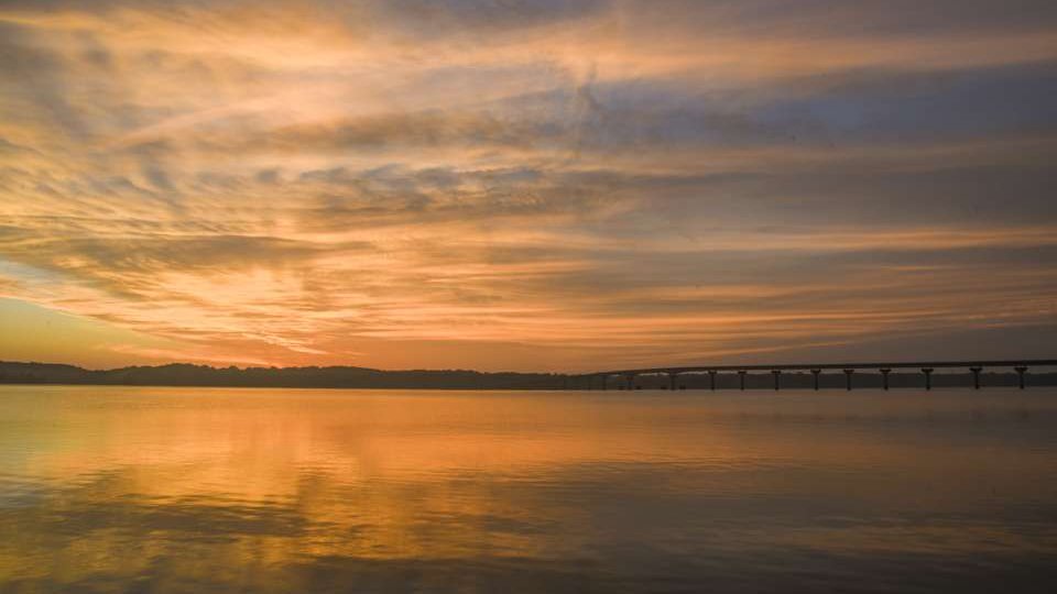 Sunset over a calm lake with a distant bridge and colorful sky reflections.