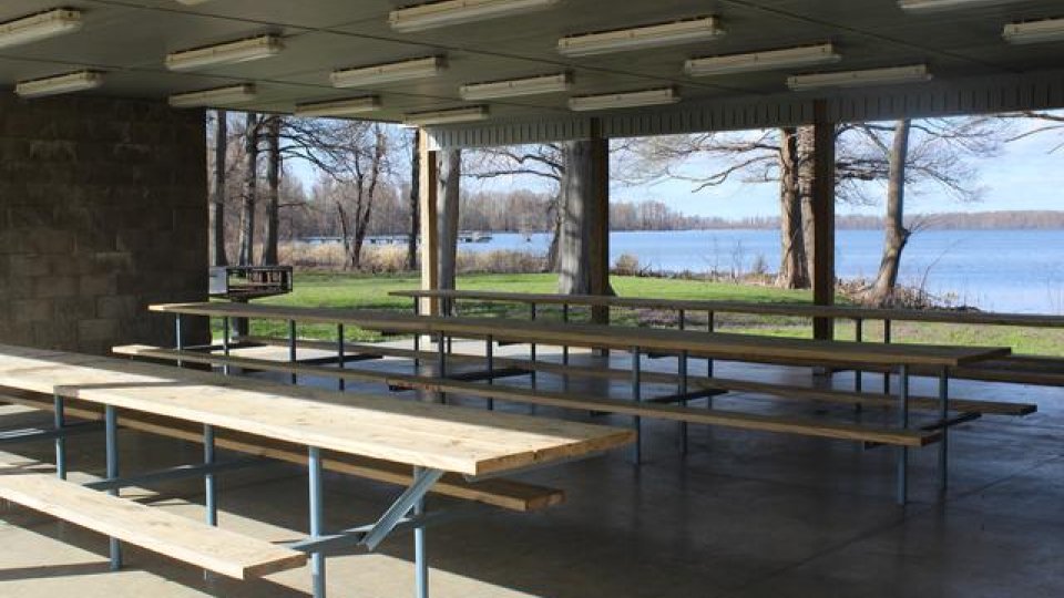 Covered pavilion with picnic tables, view of lake and trees beyond.
