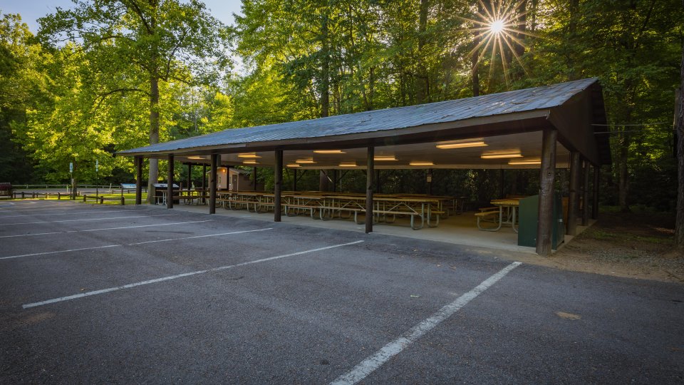 Outdoor pavilion by forest, sunlight peeking through trees.