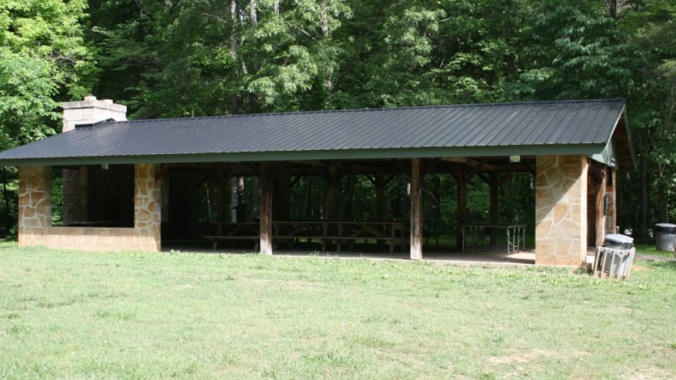 Outdoor pavilion with a black roof, surrounded by trees.