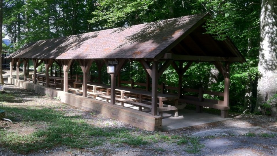 Outdoor picnic shelter with wooden benches in a forested park setting.