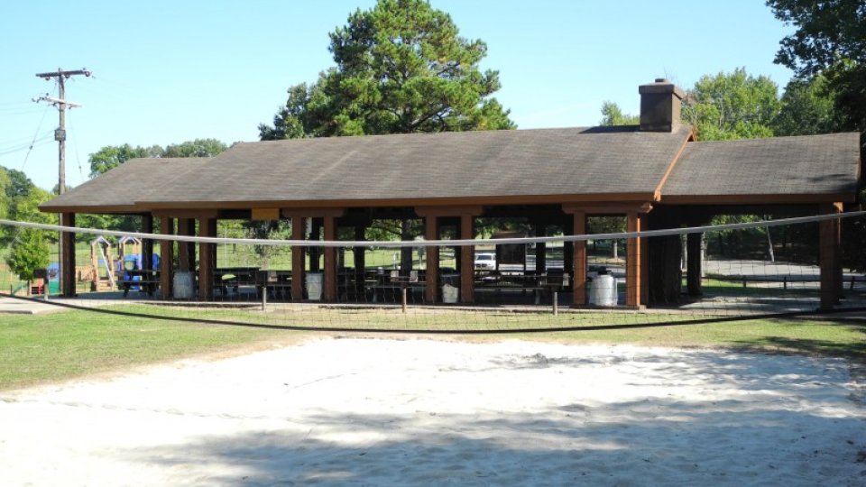 Pavilion with tables, surrounded by trees and a sandy foreground.