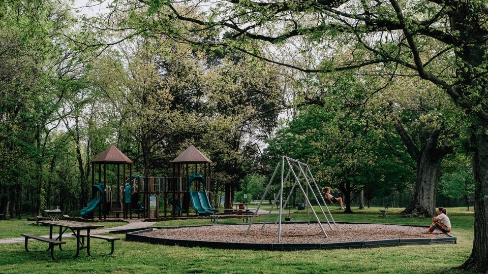 Park playground with slides, swings, picnic tables, and lush green trees.