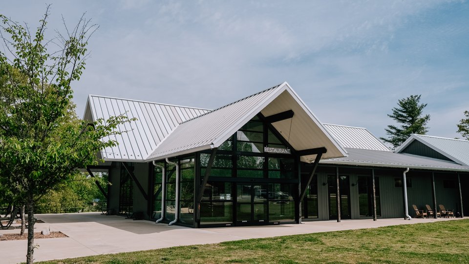 Modern restaurant with triangular roof, glass entrance, and surrounding greenery.