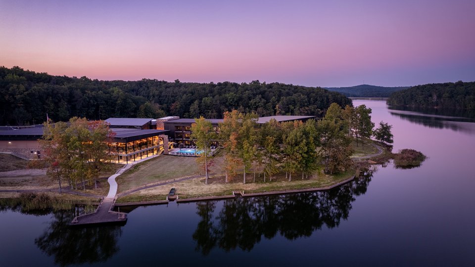 Lakeside lodge surrounded by trees at sunset.