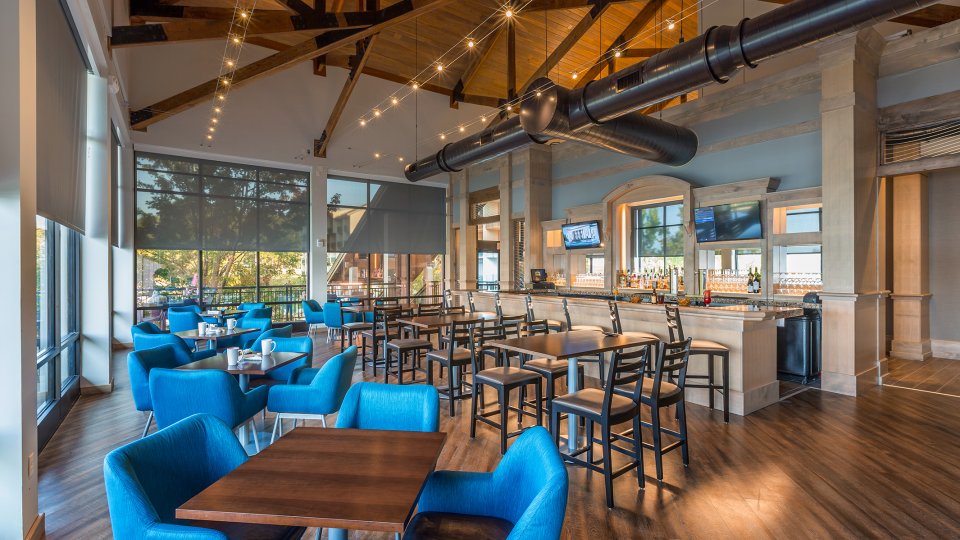 Spacious restaurant with blue chairs, wooden tables, and a bar area with high stools.