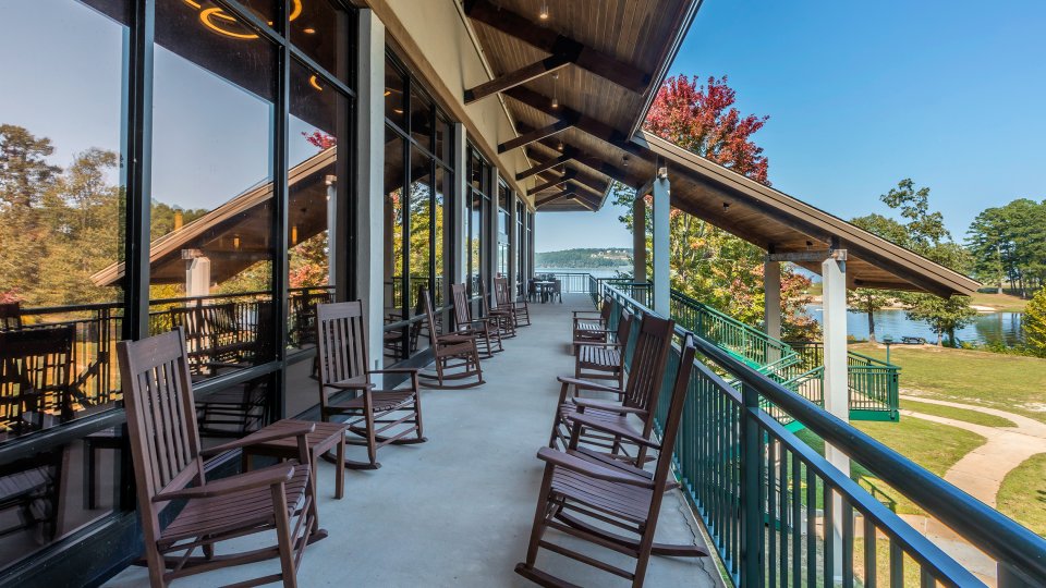 Wooden rocking chairs on a covered patio overlooking a lake.