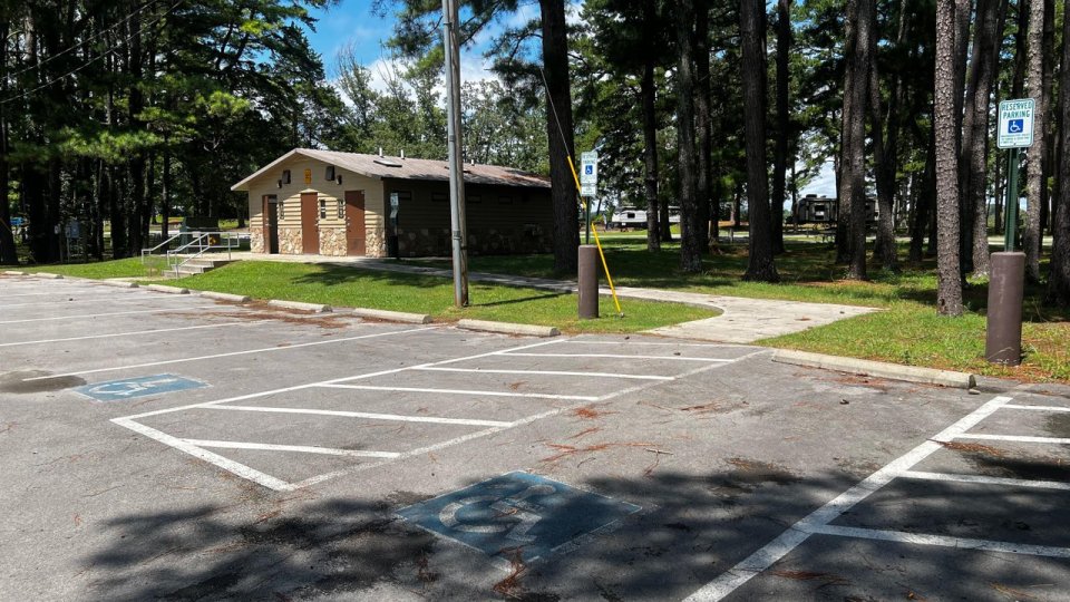 A parking area surrounded by tall trees, featuring accessible parking spaces and a restroom facility in a natural setting.
