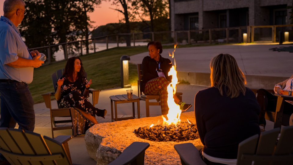 People sitting around a firepit at sunset, talking and relaxing.