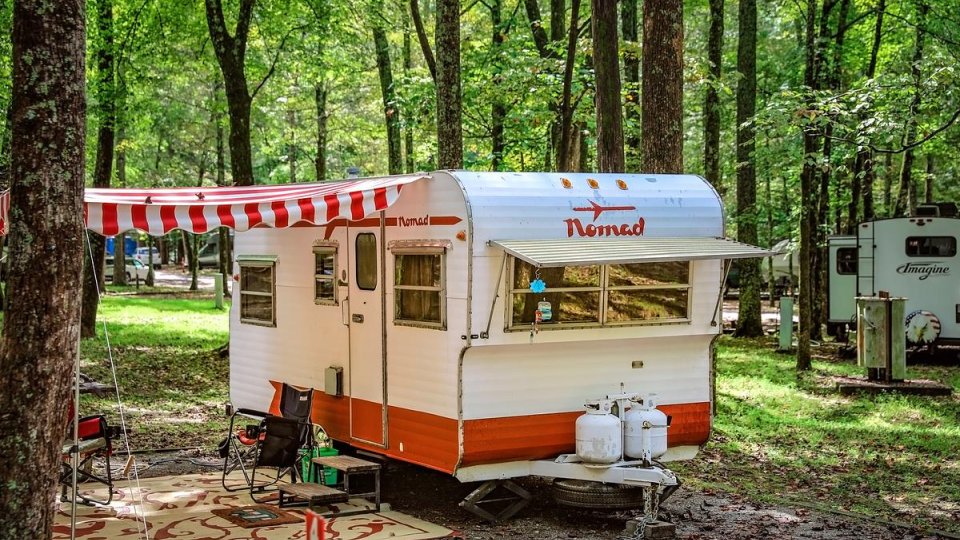 Vintage camper with striped awning in a forest campsite.