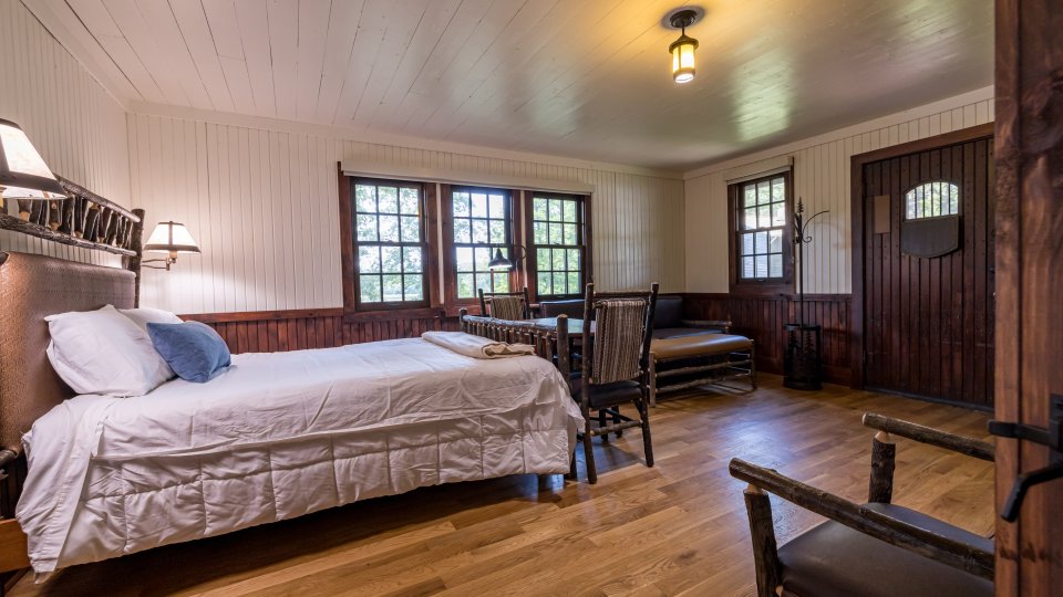 Cozy cabin room with single bed, wooden furniture, dining set, and large windows.