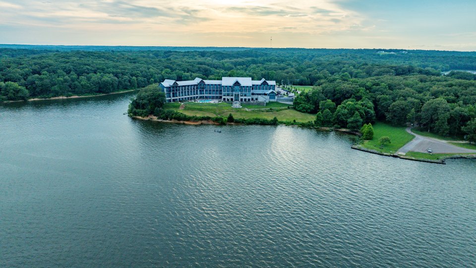 Aerial view of a lakeside lodge surrounded by trees under a cloudy sky.