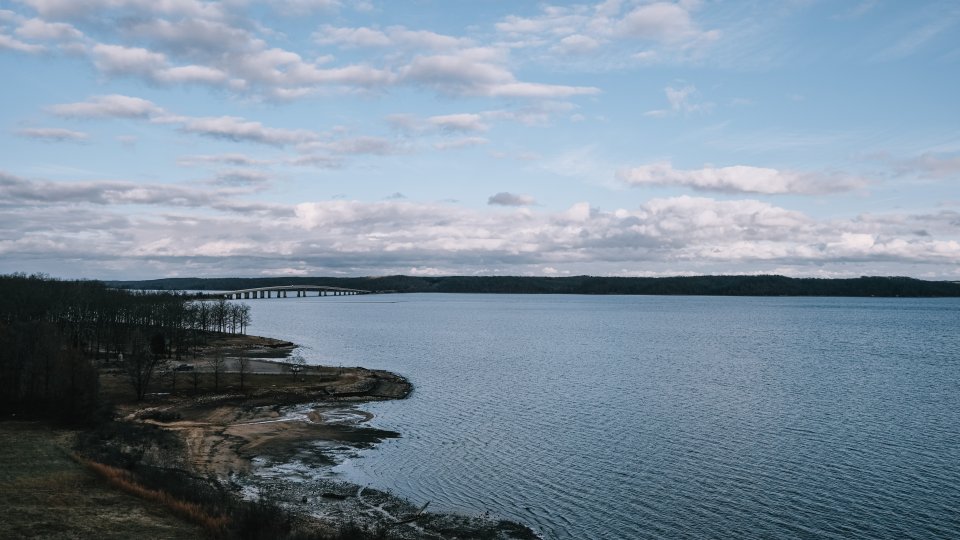 An expansive lake with the shore in frame and a bridge in the distance during winter